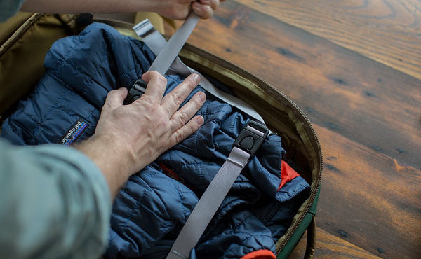 A person lashing down a padded jacket the main compartment of the Guide's Edition Synik 22 using the included tie-down straps.